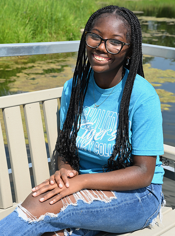 Neema sitting on a bench smiling, with the MCC pond behind her