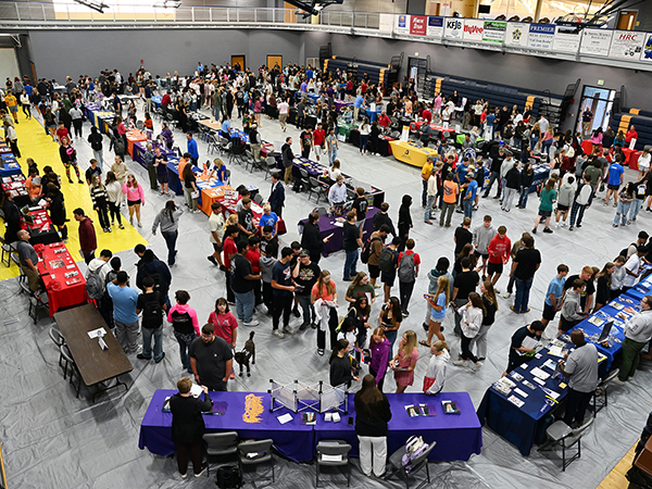 students and their parents visiting multiple colleges tables at a college fair in the MCC gym