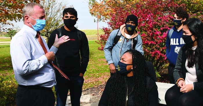 a-photo-of-students-and-a-professor-wearing-masks-outside-listening-to-a-lecture